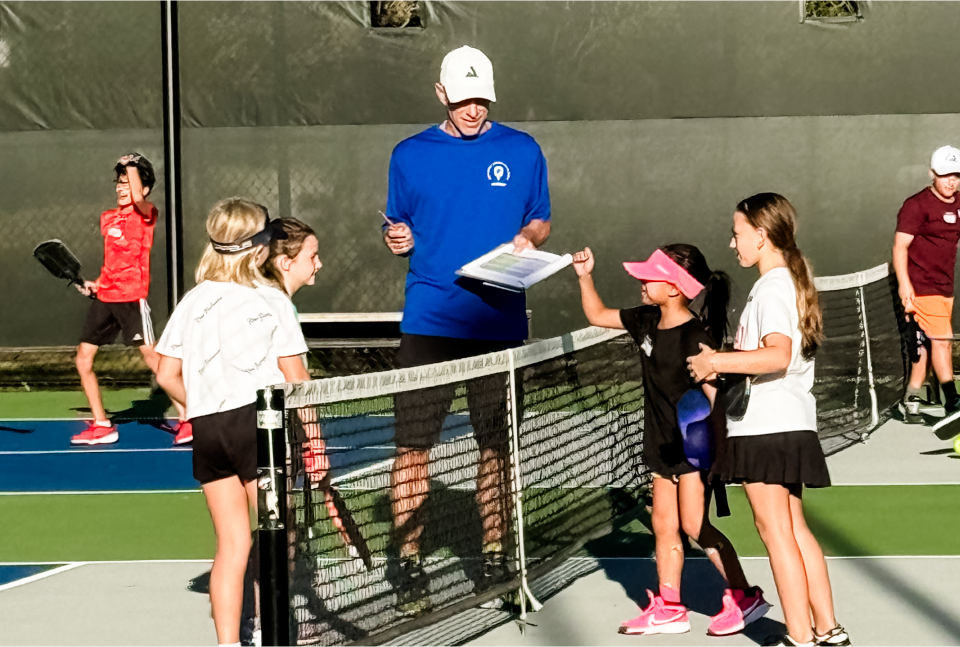 National Junior Pickleball - Coach talks to four young girls on a tennis court