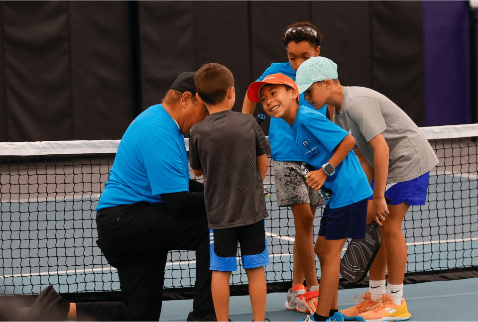 National Junior Pickleball - Coach talks to four children on a tennis court